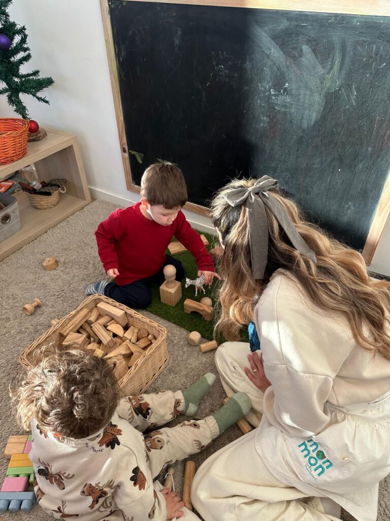 Dos niños pequeños en un ambiente Montessori de Comunidad Infantil concentrados trabajando con bloques de madera en una cesta, acompañados por una guía.