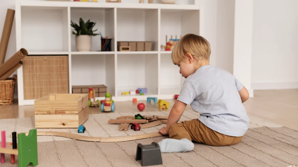 Niño jugando en el suelo con algunos juguetes de madera y un estante al fondo con unos pocos objetos. Estilo Montessori.
